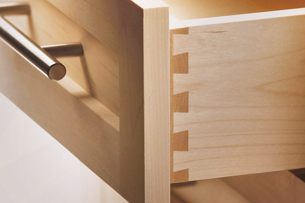 Close-up of a dovetail joint corner on a light maple drawer box with a stainless bar pull