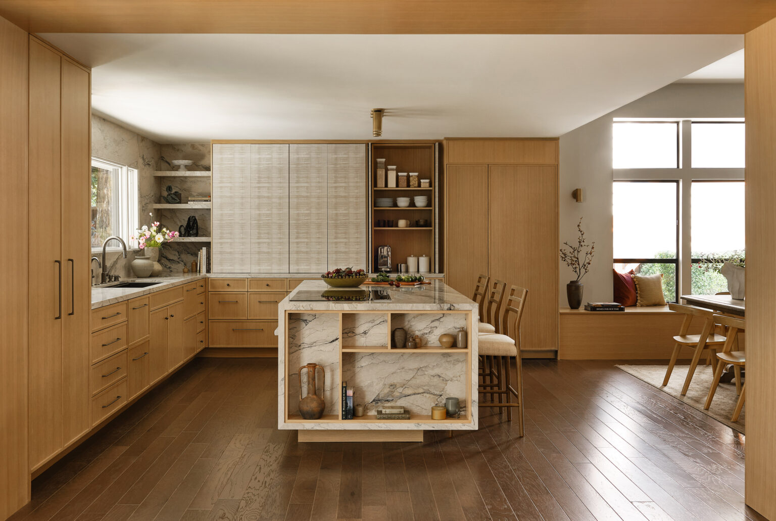 Light oak kitchen with marble waterfall island, open shelving and tall pantry cabinets